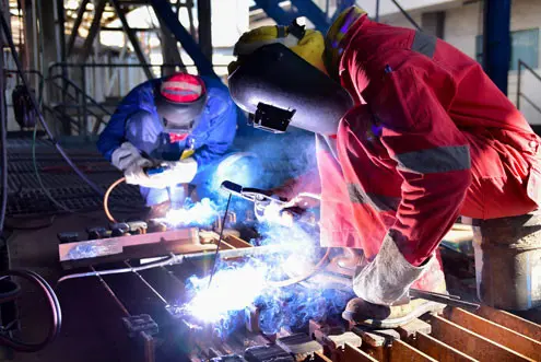 Deux soudeurs portent des chaussures de soudeur et travaillent en étant assis