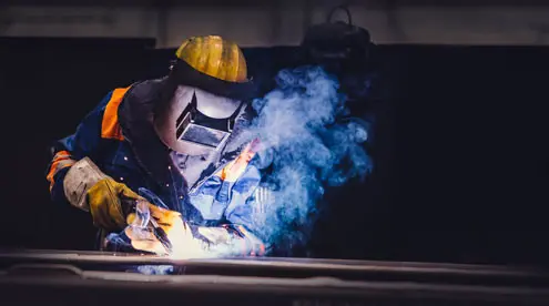 soudeur porte un masque et un casque jaune dans un atelier